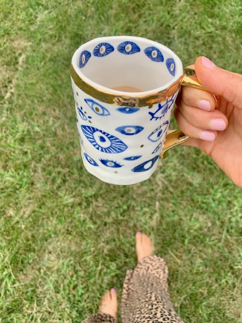 hand holding a seeing eye blue and white coffee cup while grounding in the grass