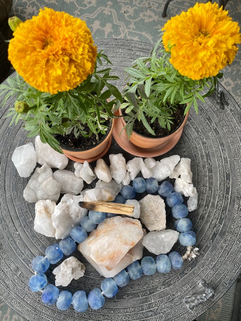 two marigolds, quartz rocks and beads with palo santos burning on top of rocks